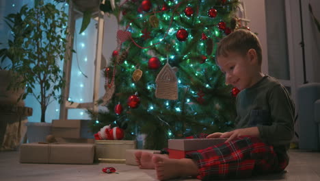 The-boy-opens-the-gift-and-the-light-from-the-box-illuminates-the-joyful-face.-Open-a-gift-under-the-tree.-High-quality-4k-footage